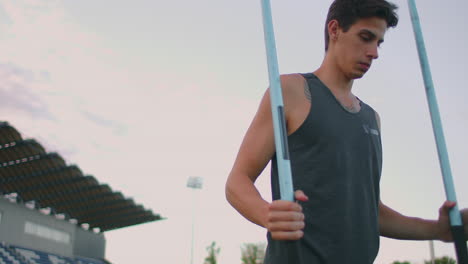Tired-javelin-thrower-a-man-at-the-stadium-collects-spears.-Preparing-for-the-all-around.-Walking-through-the-stadium-after-training-in-the-background-of-the-stands-and-carrying-spears-for-throwing.